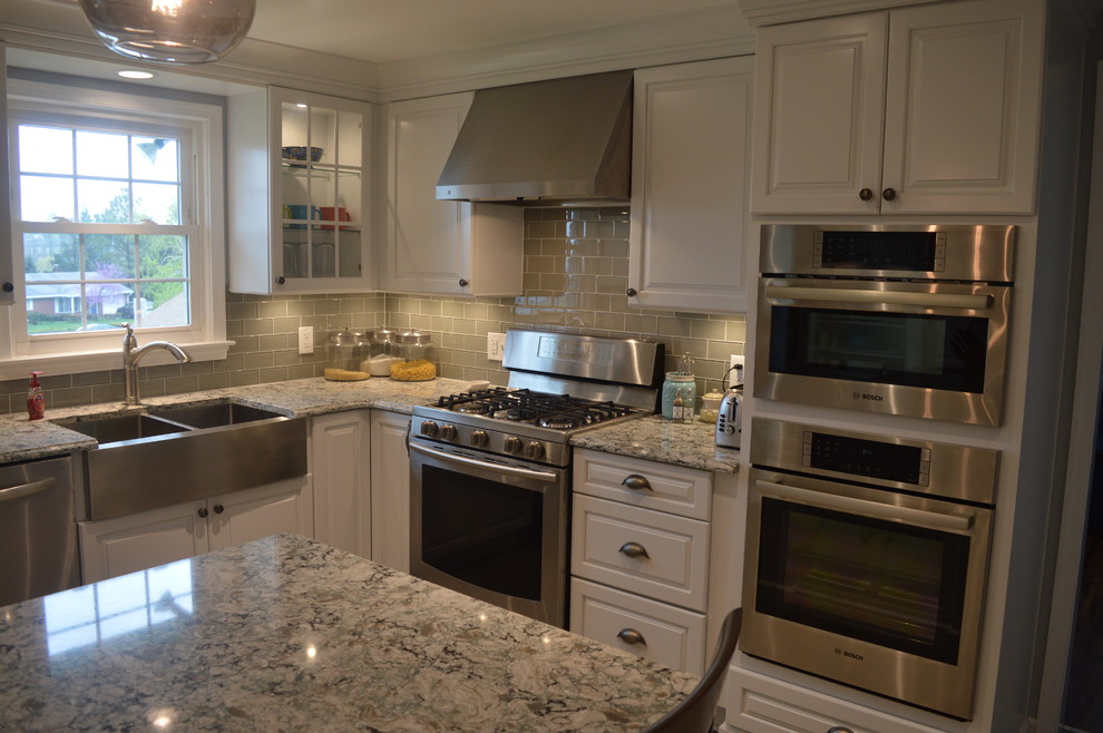 Enclosed kitchen - large transitional u-shaped ceramic tile and gray floor enclosed kitchen idea with a farmhouse sink, raised-panel cabinets, white cabinets, quartz countertops, gray backsplash, glass tile backsplash, stainless steel appliances and an island