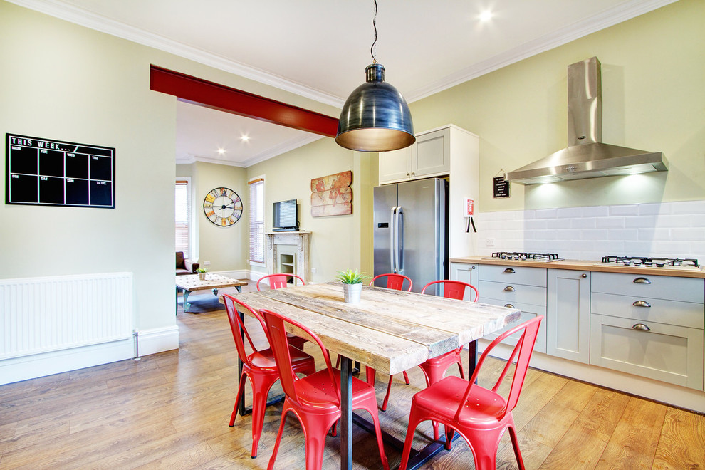 Large country l-shaped eat-in kitchen in London with a double-bowl sink, shaker cabinets, grey cabinets, white splashback, subway tile splashback, stainless steel appliances and light hardwood floors.