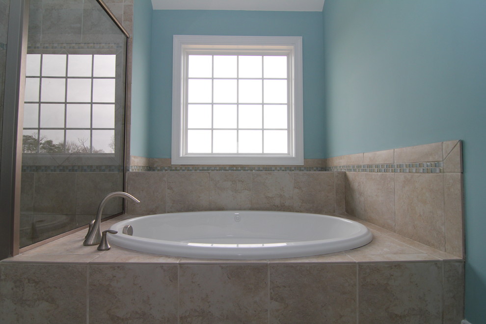 Photo of a large beach style ensuite bathroom in Raleigh with raised-panel cabinets, medium wood cabinets, a built-in bath, a corner shower, a one-piece toilet, blue tiles, blue walls and ceramic flooring.