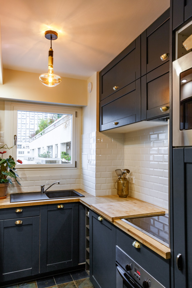 パリにある小さなトロピカルスタイルのおしゃれなL型キッチン (アンダーカウンターシンク、青いキャビネット、木材カウンター、白いキッチンパネル、サブウェイタイルのキッチンパネル、シルバーの調理設備、青い床、ベージュのキッチンカウンター) の写真