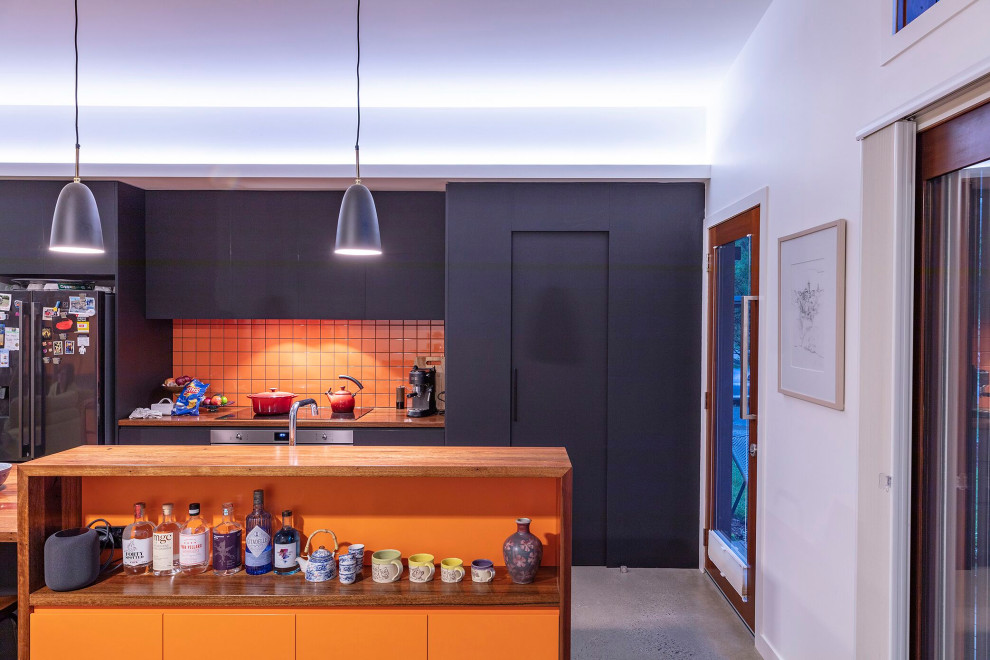 This is an example of a small contemporary galley open plan kitchen in Canberra - Queanbeyan with a drop-in sink, flat-panel cabinets, black cabinets, wood benchtops, orange splashback, porcelain splashback, stainless steel appliances, concrete floors, with island and grey floor.