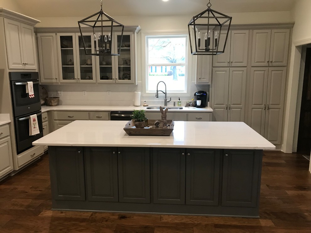 Example of a large transitional l-shaped dark wood floor and brown floor open concept kitchen design with a double-bowl sink, raised-panel cabinets, gray cabinets, white backsplash, subway tile backsplash, stainless steel appliances, an island and white countertops
