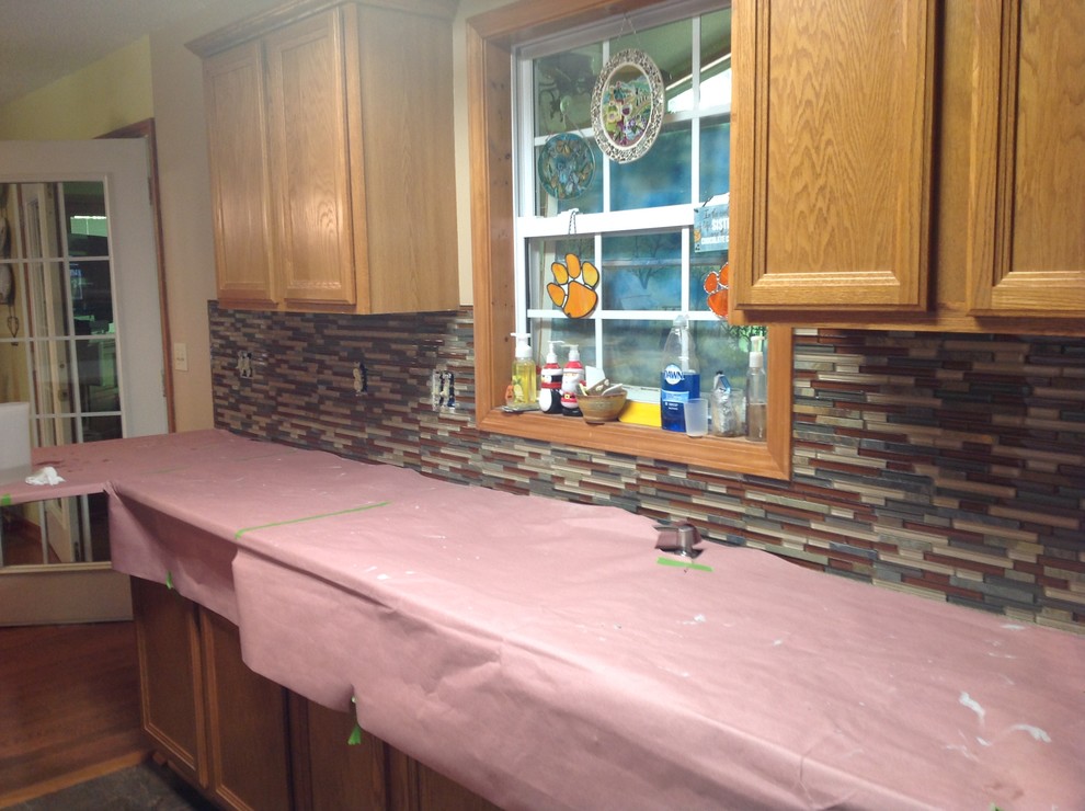 Eat-in kitchen - l-shaped eat-in kitchen idea with an undermount sink, flat-panel cabinets, brown backsplash, glass tile backsplash, stainless steel appliances and a peninsula