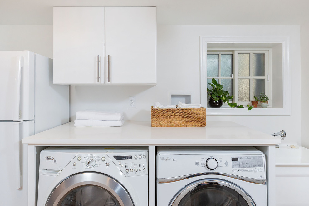 Mid-sized modern single-wall laundry room in Philadelphia with flat-panel cabinets, white cabinets, white walls, medium hardwood floors, brown floor and white benchtop.