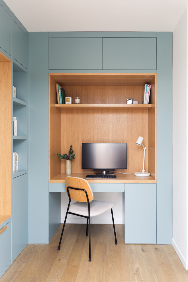 Mittelgroßes Skandinavisches Arbeitszimmer ohne Kamin mit Arbeitsplatz, blauer Wandfarbe, hellem Holzboden und Einbau-Schreibtisch in Paris