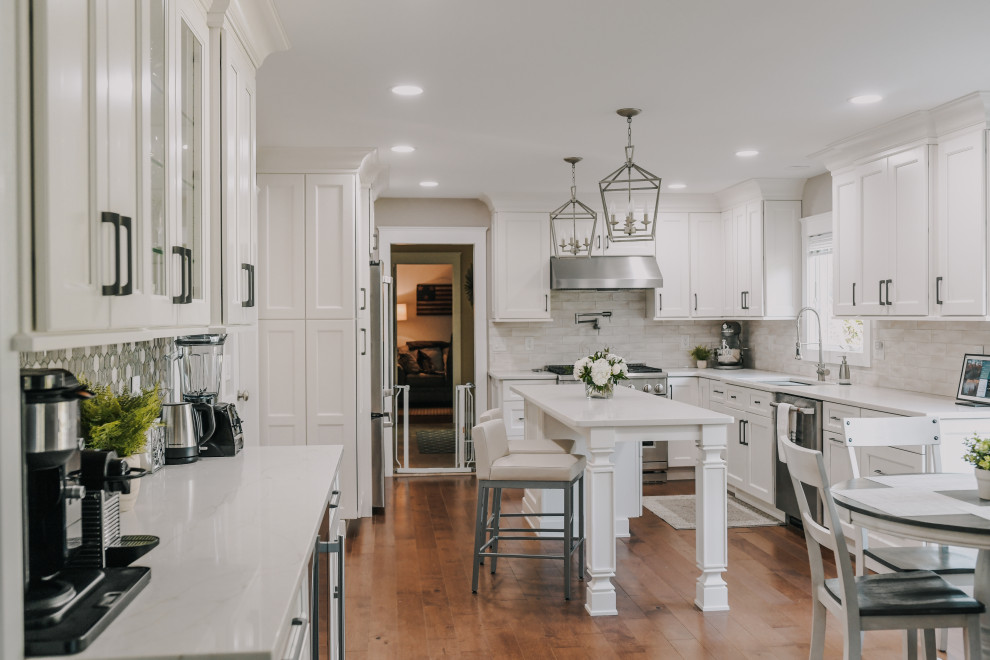 Photo of a transitional u-shaped eat-in kitchen in Other with an undermount sink, shaker cabinets, white cabinets, beige splashback, stainless steel appliances, medium hardwood floors, with island, brown floor and white benchtop.