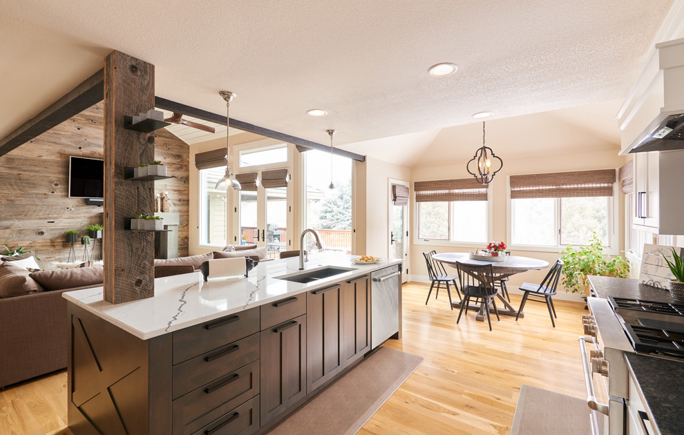 This is an example of a large contemporary l-shaped open plan kitchen in Denver with an undermount sink, shaker cabinets, brown cabinets, quartz benchtops, black splashback, ceramic splashback, stainless steel appliances, light hardwood floors, with island, brown floor and white benchtop.