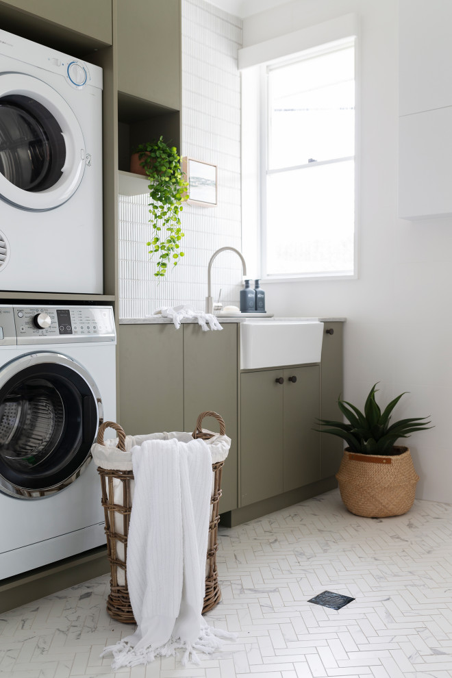 Inspiration for a mid-sized transitional single-wall laundry room in Canberra - Queanbeyan with a farmhouse sink, green cabinets, quartz benchtops, white walls, a stacked washer and dryer, flat-panel cabinets, white splashback, matchstick tile splashback, white floor and white benchtop.