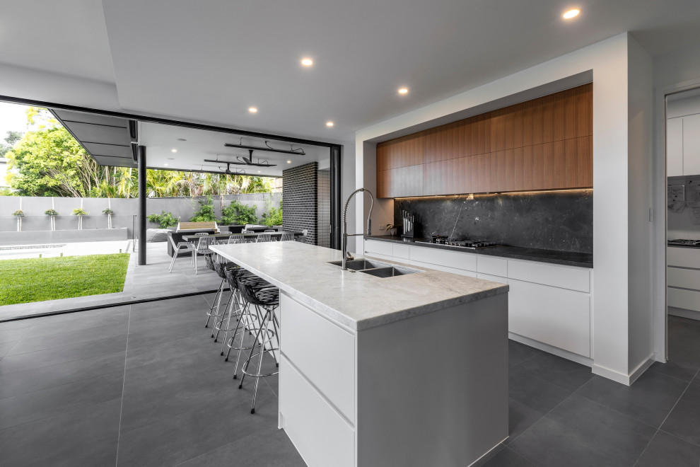 Inspiration for a contemporary galley open plan kitchen with an undermount sink, white cabinets, marble benchtops, black splashback, marble splashback, ceramic floors, with island, grey floor and black benchtop.