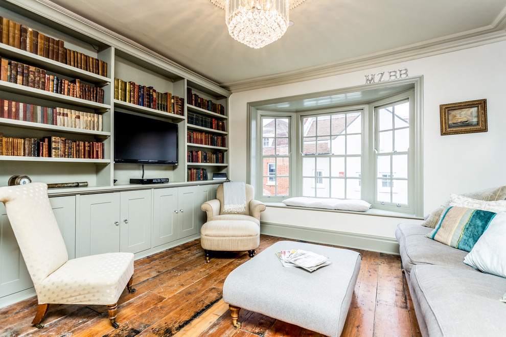 Traditional living room in Hampshire with a library, green walls, medium hardwood floors and a wall-mounted tv.
