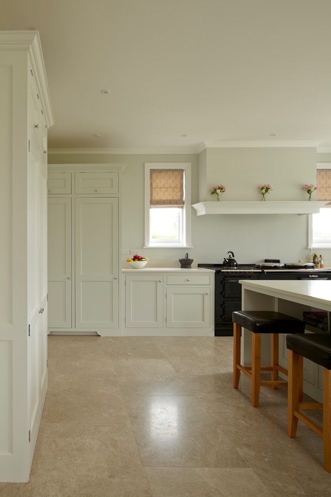 Design ideas for a mid-sized traditional l-shaped open plan kitchen in Hampshire with a farmhouse sink, shaker cabinets, white cabinets, quartzite benchtops, black appliances, limestone floors, with island, beige floor and white benchtop.