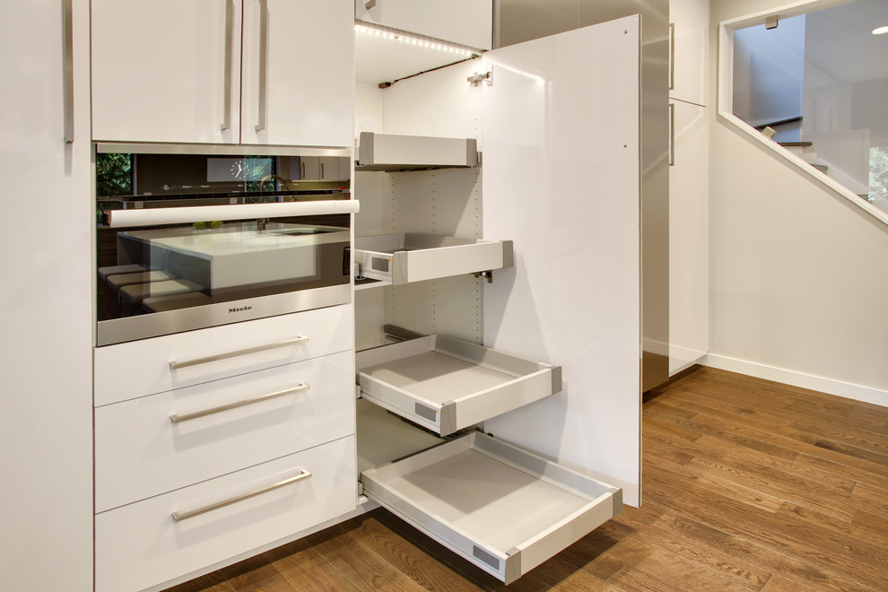 Mid-sized contemporary l-shaped separate kitchen in Seattle with an undermount sink, flat-panel cabinets, white cabinets, quartz benchtops, beige splashback, glass tile splashback, stainless steel appliances, medium hardwood floors and with island.