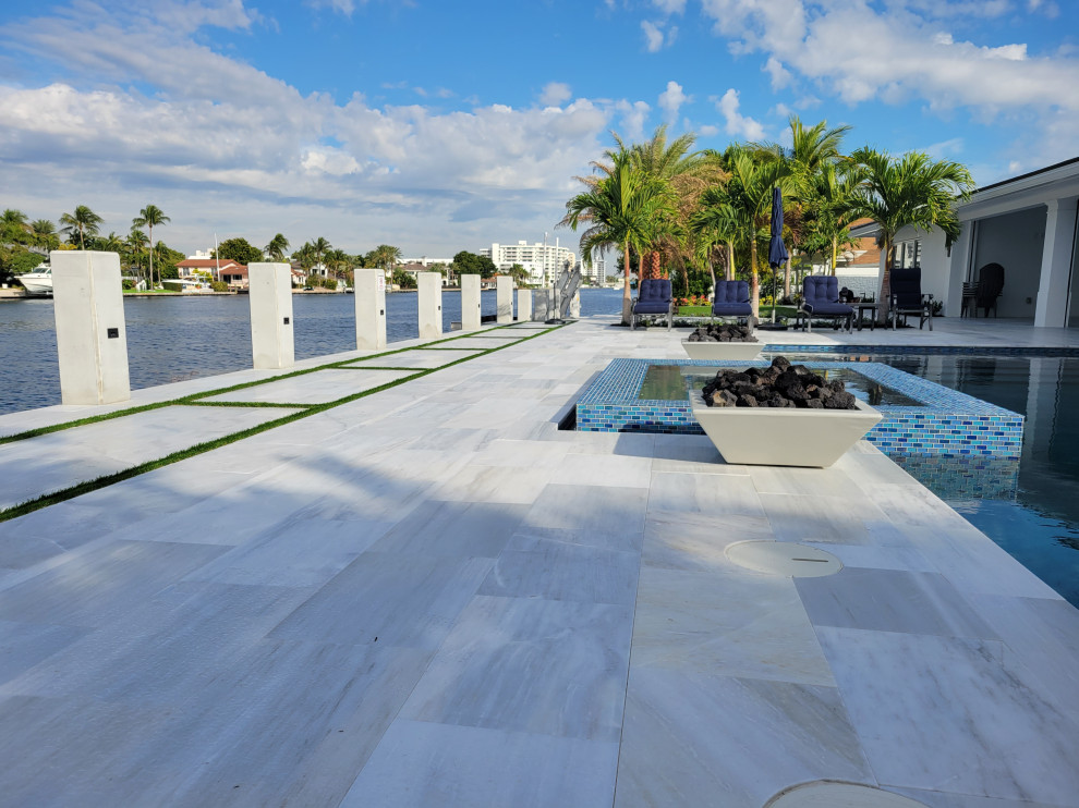 Réalisation d'un très grand piscine avec aménagement paysager arrière rectangle avec des pavés en pierre naturelle.
