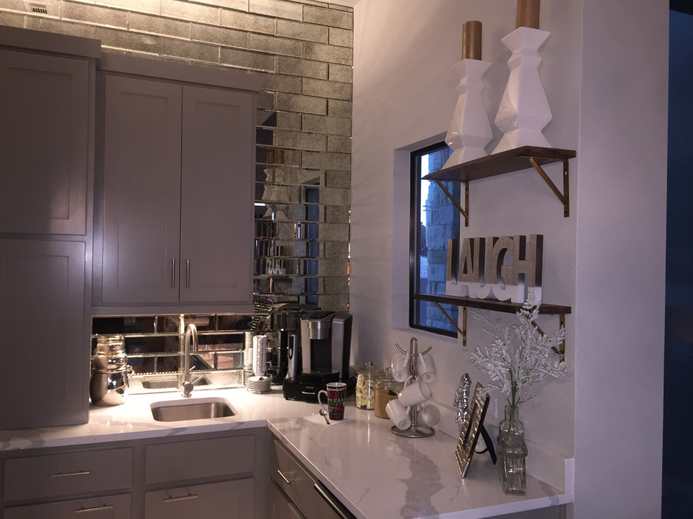 Example of a small transitional l-shaped porcelain tile and beige floor wet bar design with an undermount sink, shaker cabinets, gray cabinets, quartzite countertops, mirror backsplash and white countertops