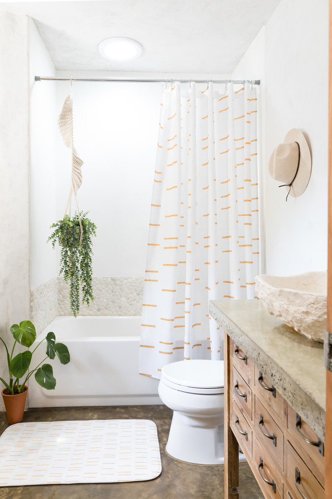 Photo of a beach style bathroom in Denver with medium wood cabinets, an alcove tub, a shower/bathtub combo, beige tile, pebble tile, white walls, concrete floors, a vessel sink, concrete benchtops, grey floor, a shower curtain, grey benchtops and flat-panel cabinets.