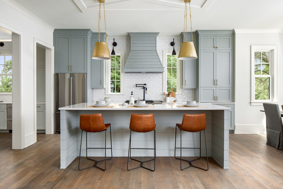 Design ideas for a country galley kitchen in Charlotte with shaker cabinets, white splashback, subway tile splashback, stainless steel appliances, medium hardwood floors, with island, brown floor, white benchtop and grey cabinets.