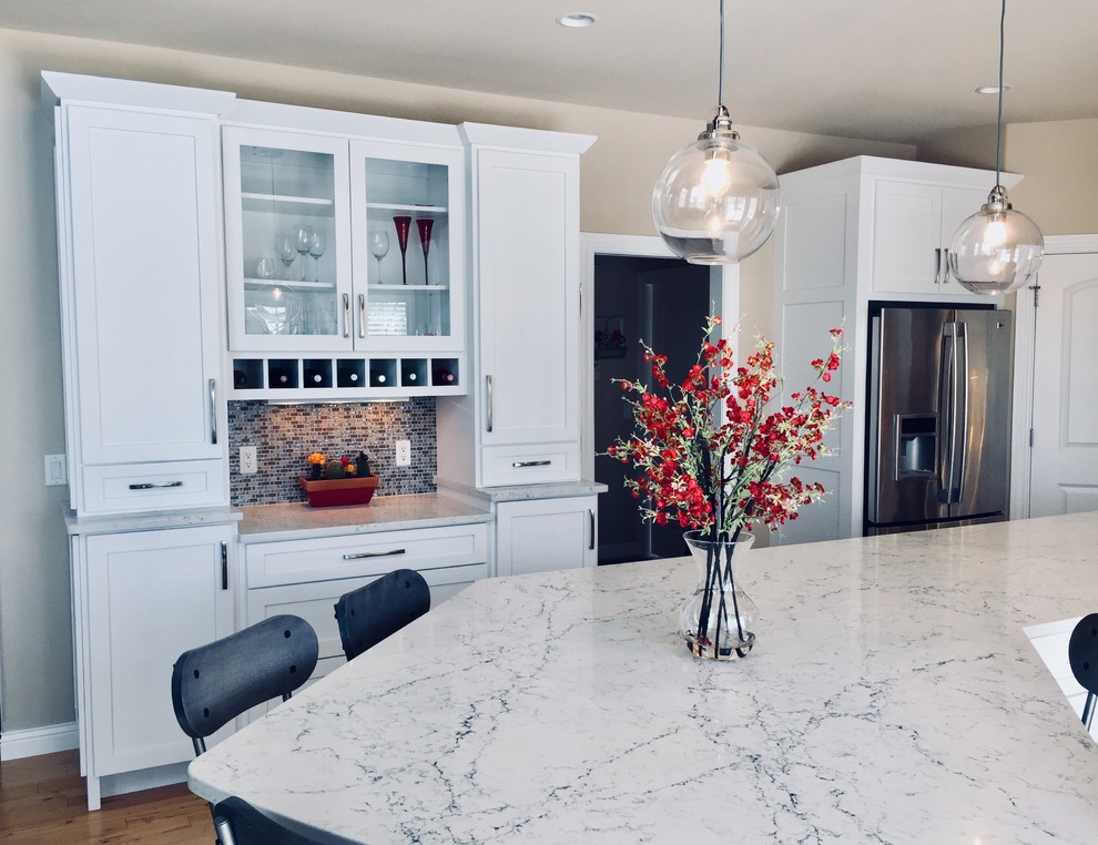 Example of a mid-sized transitional light wood floor kitchen design with an undermount sink, shaker cabinets, white cabinets, quartz countertops, blue backsplash, glass tile backsplash, stainless steel appliances and an island