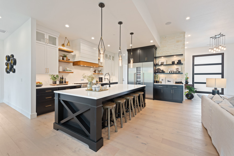Photo of a transitional l-shaped open plan kitchen in Portland with shaker cabinets, black cabinets, white splashback, stainless steel appliances, light hardwood floors, with island, beige floor and white benchtop.