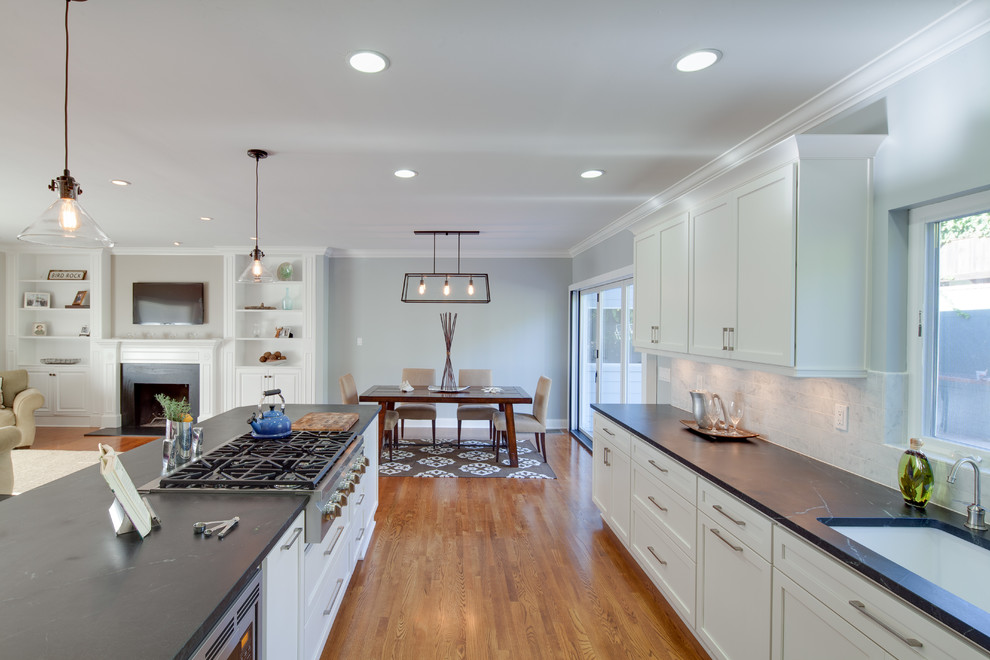 This is an example of a traditional u-shaped eat-in kitchen in San Diego with a drop-in sink, glass-front cabinets, white cabinets, granite benchtops, grey splashback, subway tile splashback and stainless steel appliances.
