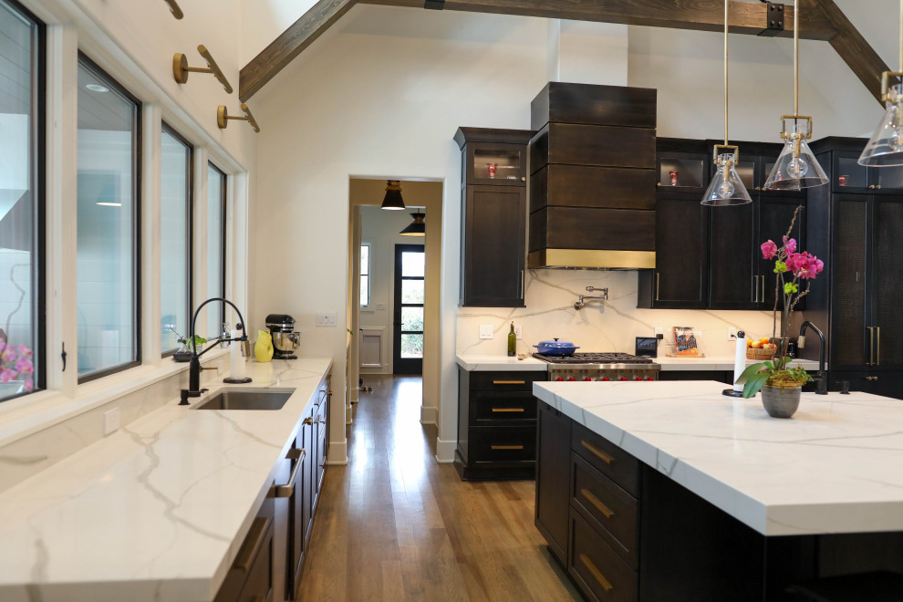 Large transitional u-shaped light wood floor open concept kitchen photo with a farmhouse sink, flat-panel cabinets, dark wood cabinets, quartz countertops, white backsplash, quartz backsplash, stainless steel appliances, an island and white countertops