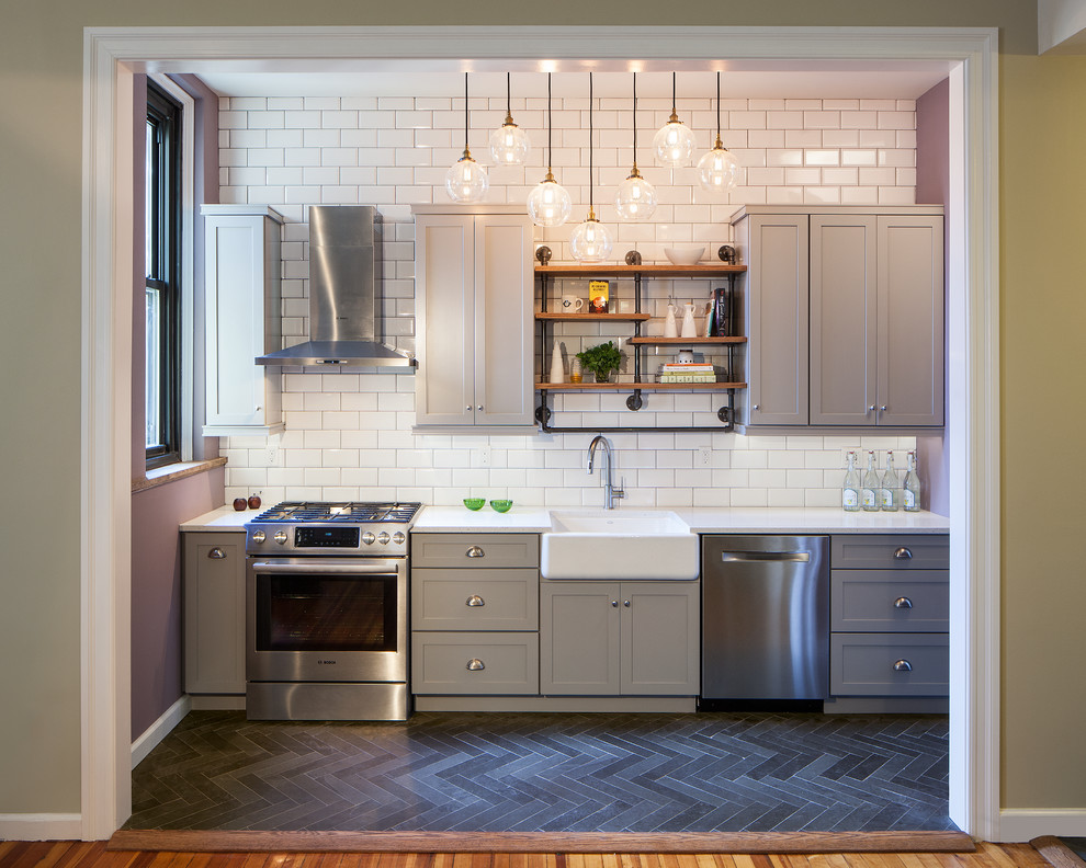 Inspiration for a transitional single-wall kitchen in New York with a farmhouse sink, shaker cabinets, grey cabinets, white splashback, subway tile splashback, stainless steel appliances, dark hardwood floors and no island.