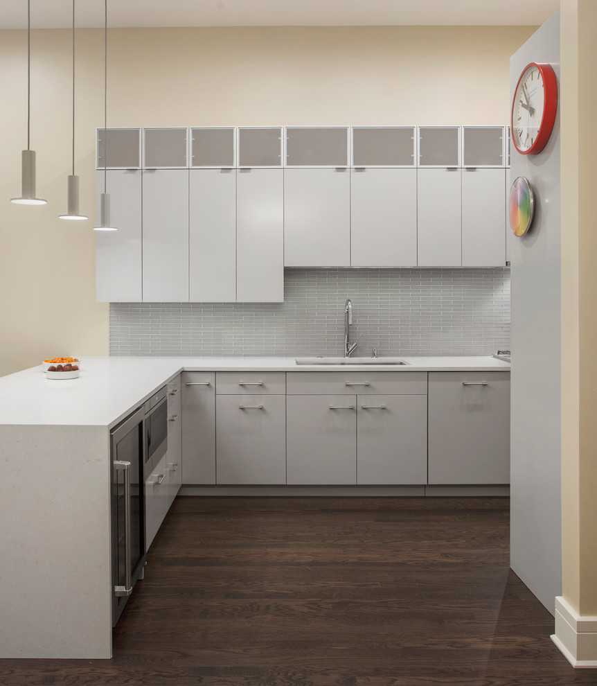 Mid-sized midcentury galley eat-in kitchen in Chicago with an undermount sink, flat-panel cabinets, grey cabinets, quartz benchtops, grey splashback, glass tile splashback, stainless steel appliances, dark hardwood floors, a peninsula and brown floor.