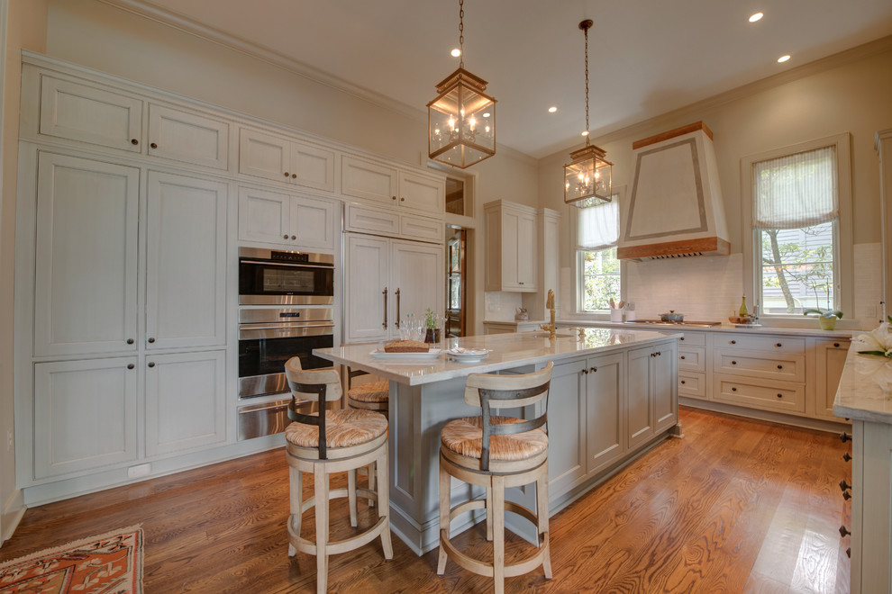 This is an example of a large traditional u-shaped separate kitchen in New Orleans with an undermount sink, recessed-panel cabinets, grey cabinets, stainless steel appliances, medium hardwood floors, with island, white splashback and brown floor.