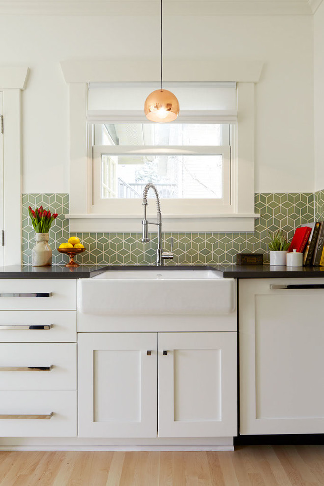 This is an example of an arts and crafts galley kitchen in Seattle with a farmhouse sink, shaker cabinets, white cabinets, quartzite benchtops, green splashback, ceramic splashback, stainless steel appliances, light hardwood floors and no island.