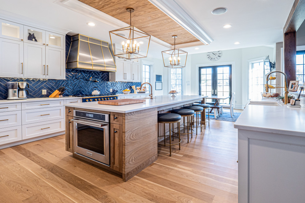 Design ideas for a large transitional u-shaped open plan kitchen in Philadelphia with a farmhouse sink, flat-panel cabinets, quartzite benchtops, blue splashback, porcelain splashback, stainless steel appliances, light hardwood floors, with island, white benchtop and coffered.