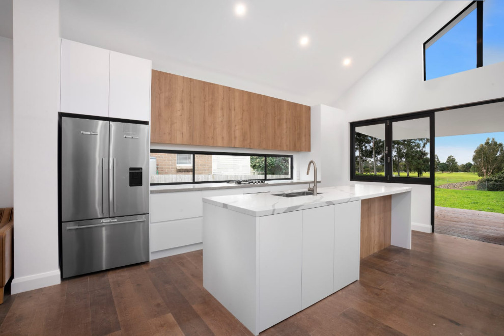 Photo of a large midcentury single-wall open plan kitchen in Sydney with a double-bowl sink, white cabinets, quartz benchtops, window splashback, stainless steel appliances, medium hardwood floors, with island, brown floor, grey benchtop and vaulted.