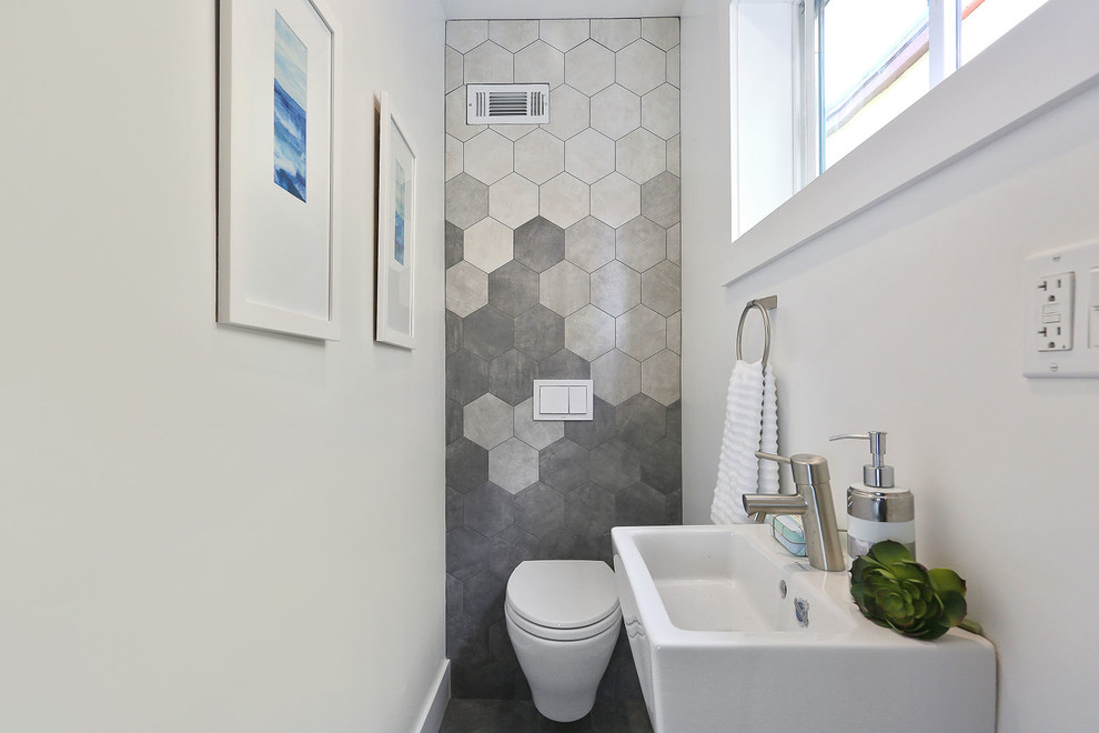 This is an example of a small modern powder room in San Francisco with a wall-mount toilet, gray tile, white walls and a wall-mount sink.