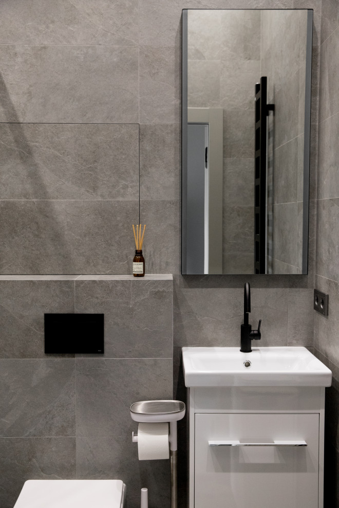 Идея дизайна: серо-белая ванная комната среднего размера в скандинавском стиле с плоскими фасадами, белыми фасадами, душем в нише, инсталляцией, серой плиткой, керамогранитной плиткой, серыми стенами, полом из керамогранита, душевой кабиной, серым полом, душем с раздвижными дверями, зеркалом с подсветкой, тумбой под одну раковину и подвесной тумбой