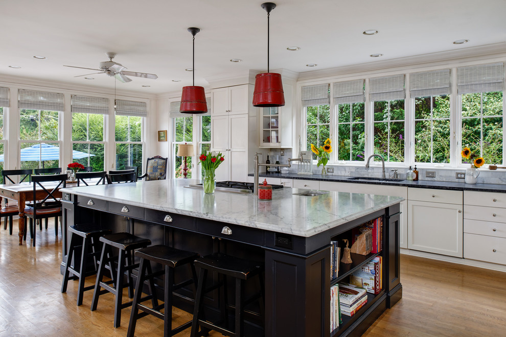 Photo of a large traditional u-shaped eat-in kitchen in DC Metro with an undermount sink, white cabinets, window splashback, medium hardwood floors, with island, shaker cabinets, soapstone benchtops, white splashback, stainless steel appliances, brown floor and black benchtop.