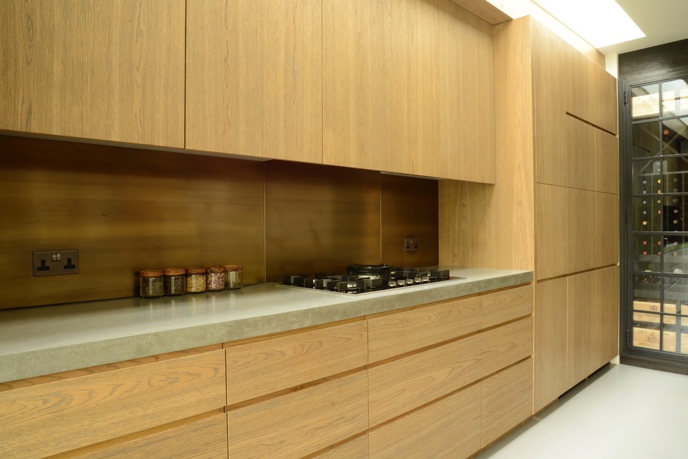 Design ideas for a mid-sized contemporary single-wall eat-in kitchen in London with an integrated sink, flat-panel cabinets, light wood cabinets, concrete benchtops, metallic splashback, metal splashback, black appliances, concrete floors and with island.