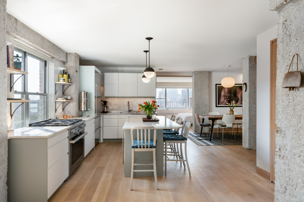 This is an example of a contemporary l-shaped kitchen in New York with an undermount sink, flat-panel cabinets, white cabinets, grey splashback, stainless steel appliances, light hardwood floors, with island, beige floor and white benchtop.