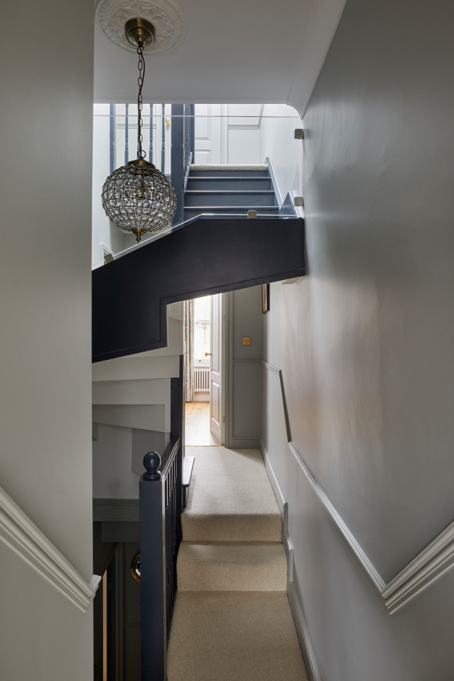 This is an example of a small transitional wood spiral staircase in London with carpet risers, wood railing and planked wall panelling.