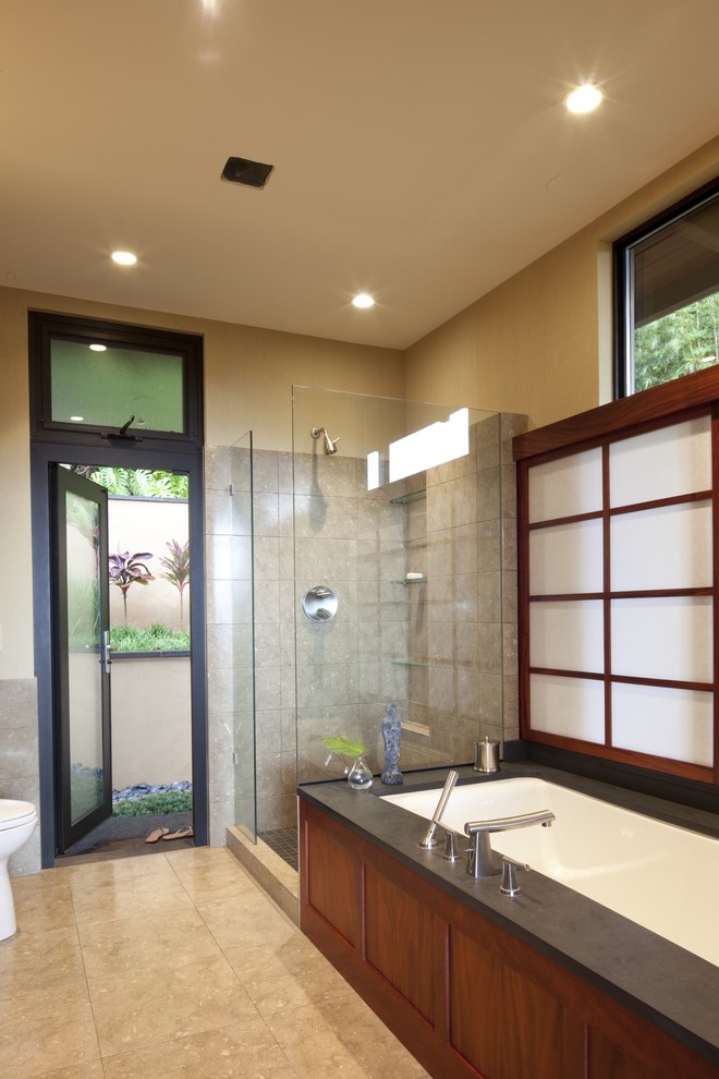 Mid-sized tropical master bathroom in Seattle with dark wood cabinets, an undermount tub, a corner shower, a two-piece toilet, gray tile, limestone, beige walls, porcelain floors, soapstone benchtops, beige floor, a hinged shower door and black benchtops.