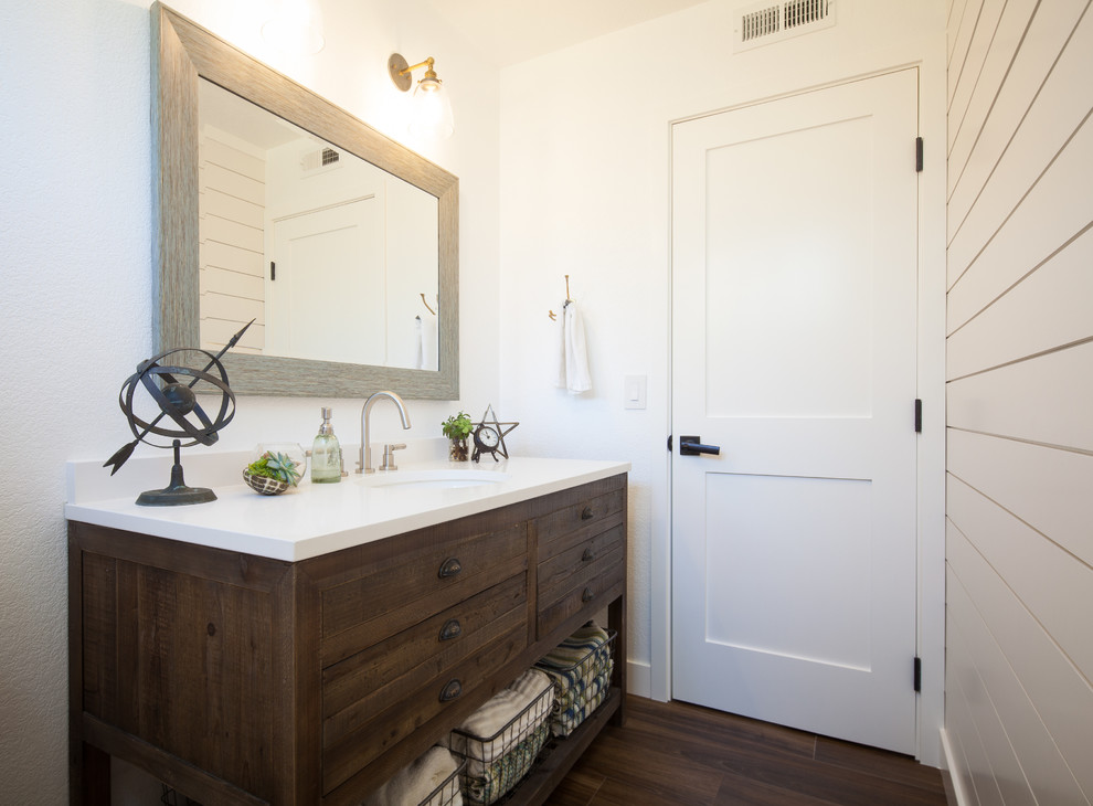 This is an example of a transitional powder room in Orange County with furniture-like cabinets, dark wood cabinets, white walls, dark hardwood floors, an undermount sink, brown floor and white benchtops.