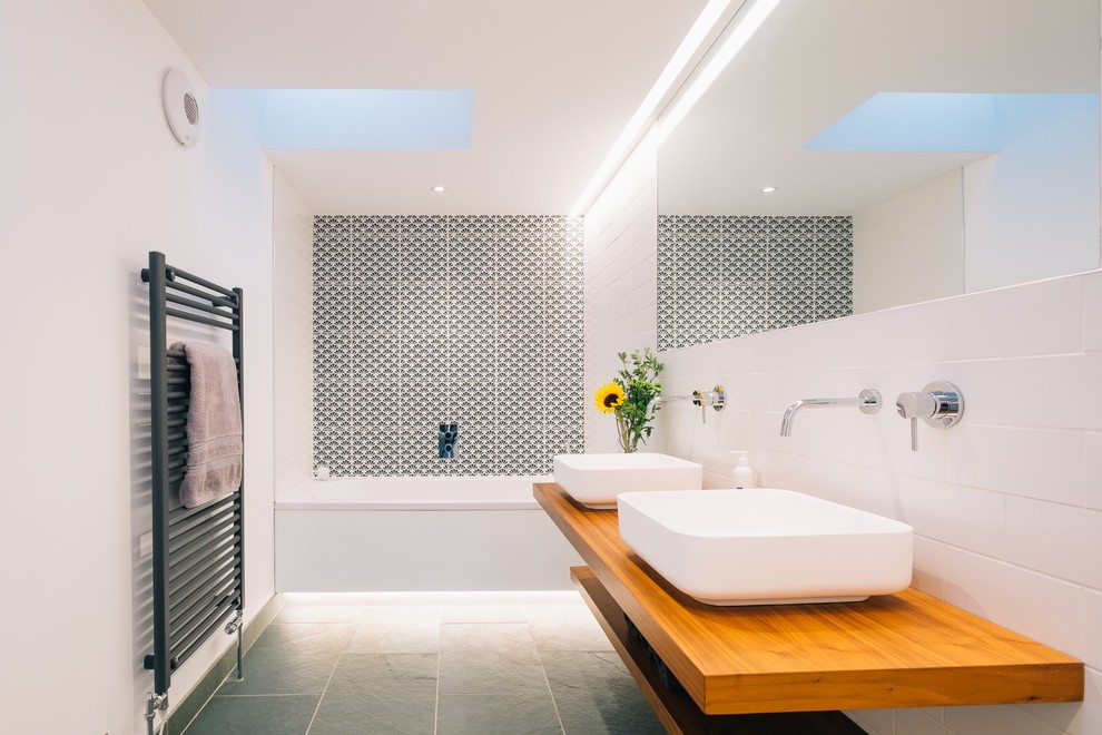 Photo of a mid-sized scandinavian bathroom in Cornwall with open cabinets, light wood cabinets, a drop-in tub, black and white tile, white tile, white walls, concrete floors, wood benchtops and brown benchtops.