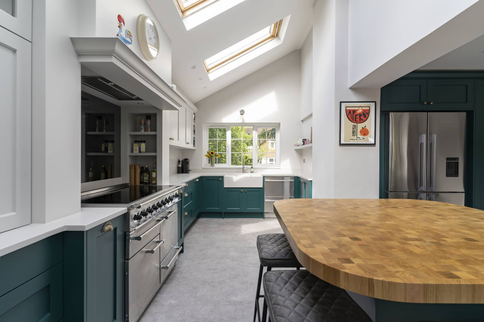 Design ideas for a large classic u-shaped kitchen/diner in Oxfordshire with a belfast sink, shaker cabinets, green cabinets, wood worktops, white splashback, stainless steel appliances, ceramic flooring, an island, grey floors, brown worktops, exposed beams and feature lighting.