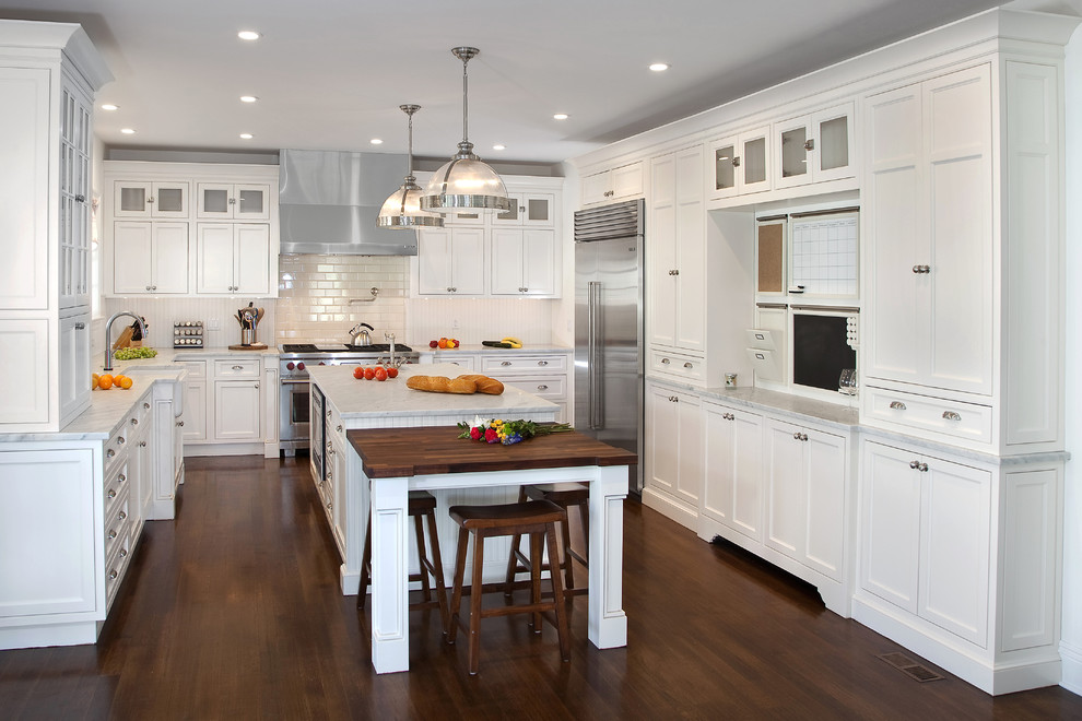 Kitchen - mid-sized traditional u-shaped dark wood floor kitchen idea in New York with a farmhouse sink, beaded inset cabinets, white cabinets, marble countertops, white backsplash, subway tile backsplash, stainless steel appliances and an island
