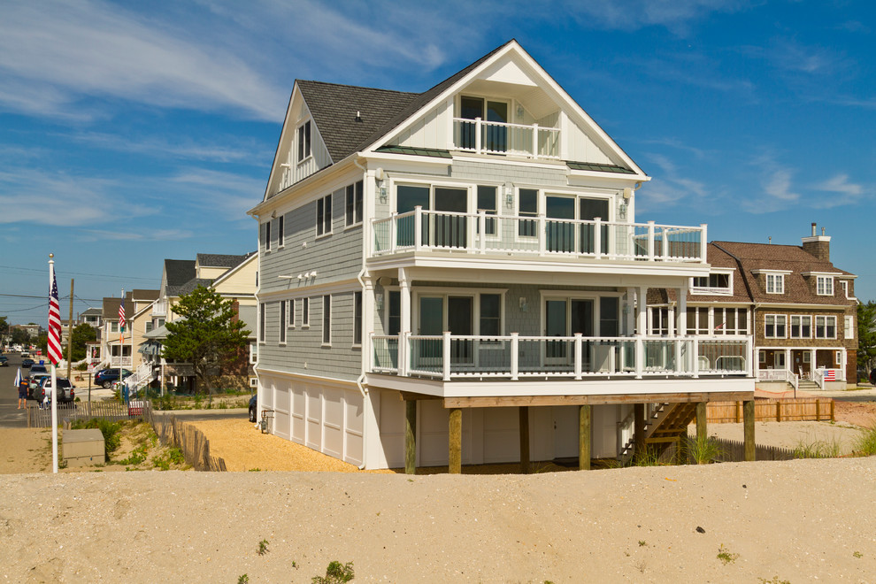 Photo of a large beach style three-storey blue house exterior in New York with vinyl siding and a shingle roof.