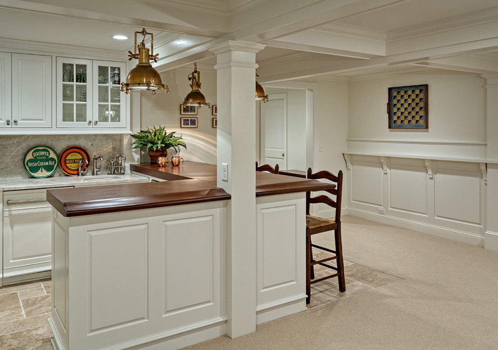 Photo of a large traditional galley seated home bar in Minneapolis with an undermount sink, raised-panel cabinets, white cabinets, wood benchtops, beige splashback, stone tile splashback, terra-cotta floors, beige floor and brown benchtop.