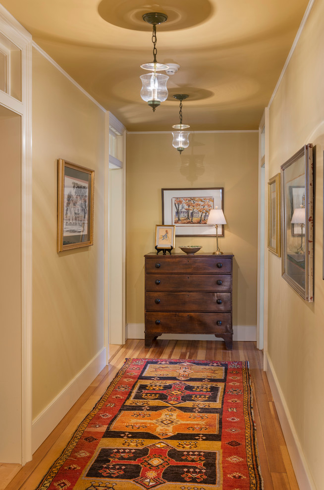 This is an example of a large country hallway in Burlington with yellow walls and light hardwood floors.
