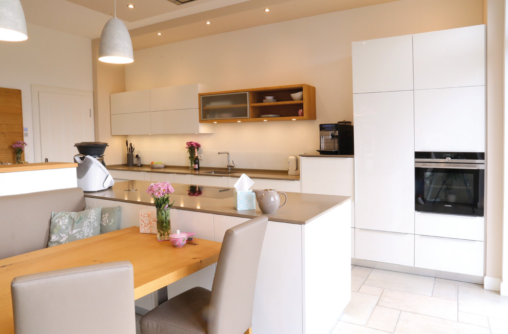 This is an example of a mid-sized contemporary galley eat-in kitchen in Bremen with an undermount sink, flat-panel cabinets, white cabinets, white splashback, panelled appliances, with island, white floor and grey benchtop.