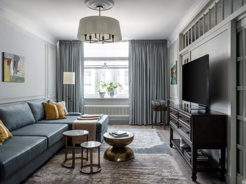 Стильный дизайн: гостиная комната среднего размера в стиле неоклассика (современная классика) с с книжными шкафами и полками, серыми стенами, светлым паркетным полом, телевизором на стене, зоной отдыха, бежевым полом, любым потолком, любой отделкой стен и синим диваном - последний тренд
