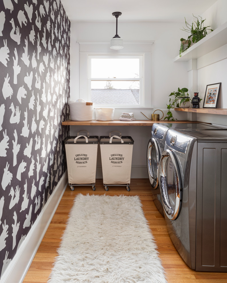 Klassisk inredning av en mellanstor bruna parallell brunt tvättstuga enbart för tvätt, med träbänkskiva, vita väggar, mellanmörkt trägolv, en tvättmaskin och torktumlare bredvid varandra och brunt golv