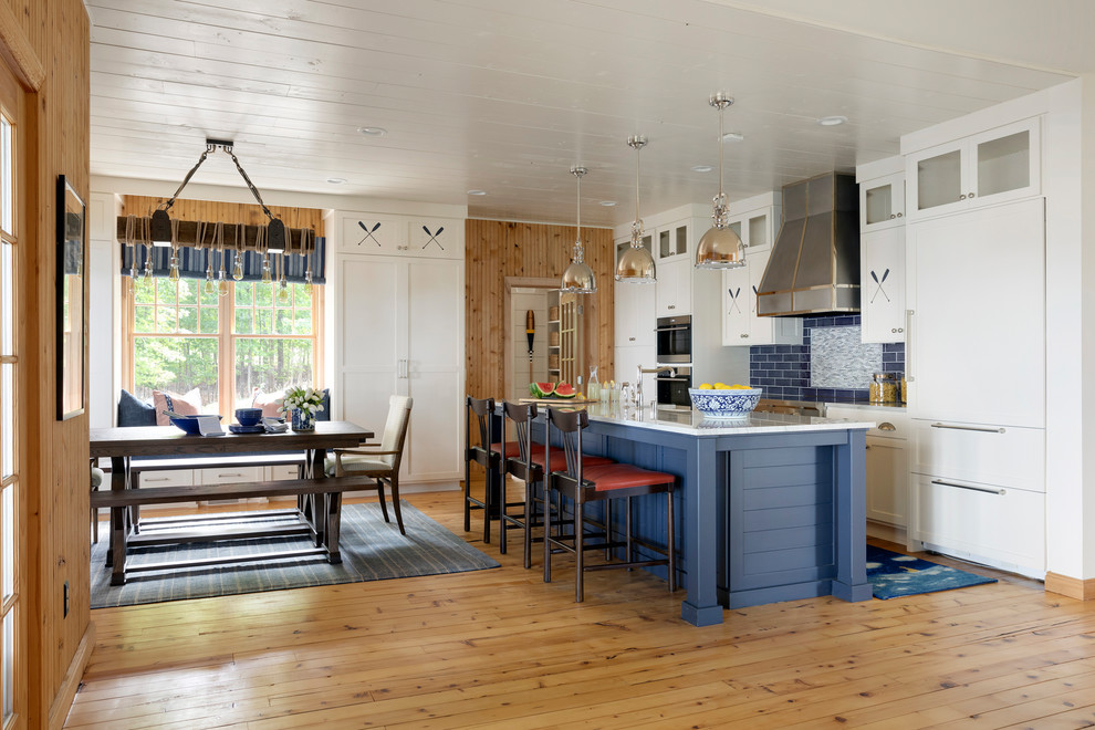 Photo of a large nautical single-wall open plan kitchen in Minneapolis with a belfast sink, shaker cabinets, white cabinets, marble worktops, blue splashback, metro tiled splashback, integrated appliances, light hardwood flooring, an island, brown floors, grey worktops and a timber clad ceiling.