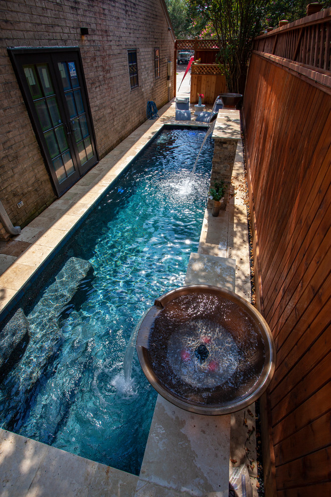 Small modern backyard rectangular lap pool in Houston with a water feature and natural stone pavers.
