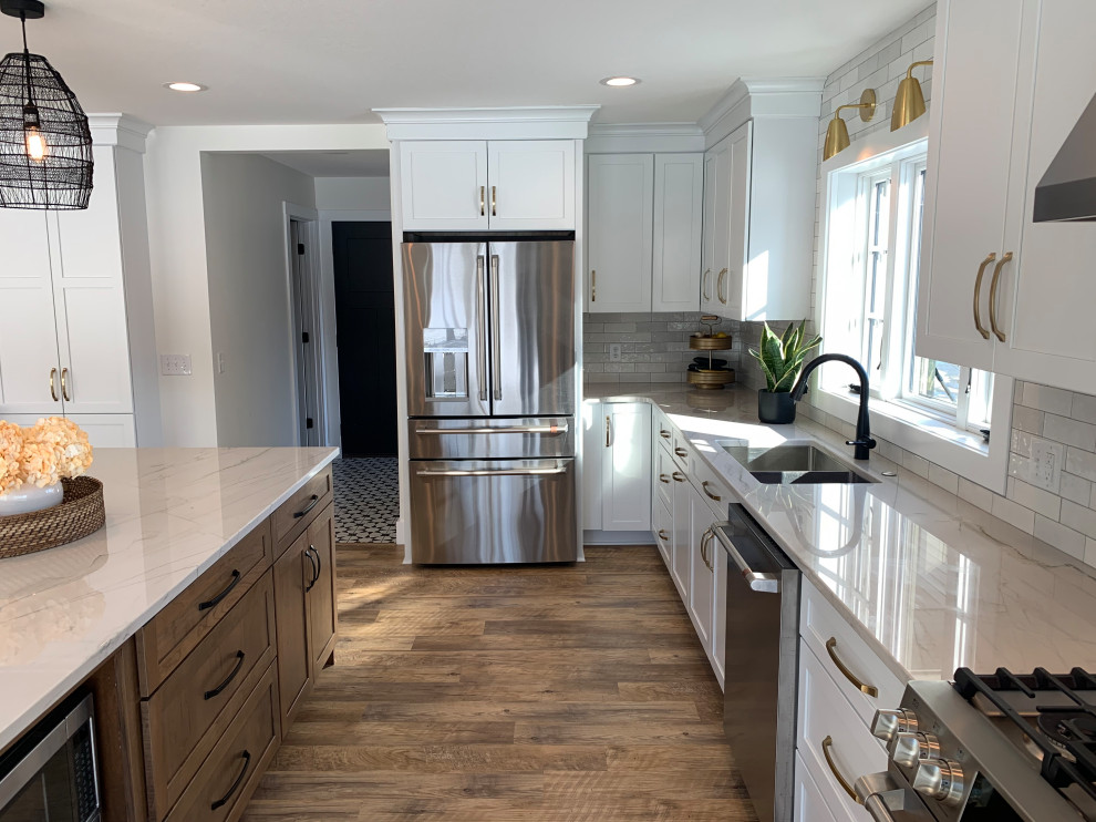 Example of a large transitional l-shaped vinyl floor and brown floor eat-in kitchen design with an undermount sink, shaker cabinets, white cabinets, quartz countertops, stainless steel appliances, an island and gray countertops